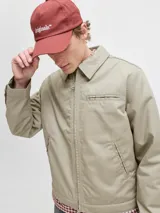 Campera tipo worker de color beige, con cuello camisero, cierre frontal completo y bolsillos laterales. Presenta un diseño minimalista y funcional con acabado limpio.