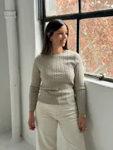 Sweater de punto color visón con diseño de trenzas verticales, cuello redondo y mangas largas.
