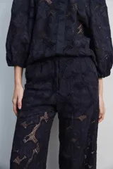 Pantalón largo negro de encaje con diseño floral calado, de tiro alto y corte recto.
