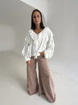 Blusa blanca de corte holgado con escote en V, decorada con volados frontales y en las mangas. Presenta mangas largas con puños elásticos y cierre frontal con botones.