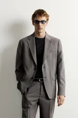 Blazer gris de corte regular fit con patrón a cuadros, confeccionada en tejido con mezcla de lana. Cuenta con cuello de solapa de muesca, cierre frontal de botonadura sencilla, bolsillos con solapa en la cadera, bolsillo de vivo en el pecho y aberturas en la espalda.
