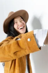 Camisa color ocre de gamuza, con cuello clásico, mangas largas con puños abotonados, cierre frontal con botones a presión y bolsillo de parche en el pecho.