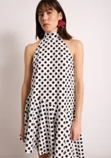 Vestido corto blanco con lunares negros, cuello halter y corte evasé.