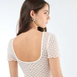 Camiseta de encaje blanco con textura de puntos, cuello redondo y mangas cortas con terminación ondulada.