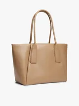 Cartera tote Tommy Hilfiger de color tostado, con acabado liso, dos asas superiores y cierre de cremallera. Cuenta con un compartimento principal, un bolsillo interior con cremallera y el logo metálico de la marca en relieve en la parte delantera.