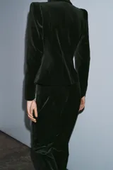 Blazer entallada de Zara Woman Collection confeccionada en tejido de terciopelo. Presenta cuello con solapas de muesca, manga larga con hombreras, bolsillos delanteros con solapa y cierre frontal con un botón. Incluye forro interior.