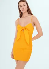 Vestido corto de tirantes finos, color amarillo, con escote recto y detalle de nudo frontal. Presenta un diseño ajustado y cierre lateral con cremallera.