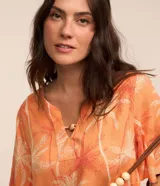 Blusa color naranja con estampado de cocoteros en blanco y rojo, cuello en V con detalle de abalorio de madera y mangas cortas acampanadas.