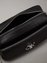 Bandolera negra de cuero sintético con correa de cadena plateada y logo CK plateado en el frente.