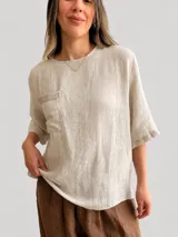Blusa de lino color blanco, con escote redondo, mangas cortas amplias, calce relajado y un bolsillo delantero con detalle de lentejuelas.