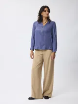 Pantalón de corte recto y pierna ancha, color beige, con cintura de tiro medio y cierre frontal.