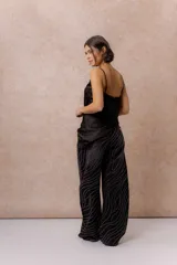 Pantalón wide leg de tiro alto en denim negro, con diseño de líneas onduladas formadas por pequeñas aplicaciones de brillos. Cuenta con cierre frontal, bolsillos funcionales y pasacintos.