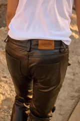 Pantalón de cuero negro con corte de jean y tiro medio, presenta apliques decorativos de rosas en la parte delantera.