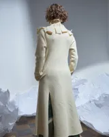 Tapado largo color natural de lana merino afieltrada, con cuello grande formado por piezas horizontales. Tiene bolsillos laterales y se puede usar suelto o cerrado con un accesorio.