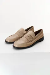 Mocasín color marrón claro, con capellada de cuero liso y aplique de gamuza en marrón oscuro. Tiene punta redondeada y suela plana de goma negra.