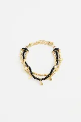 Pulsera multicapa con hilos de cuentas negras y cuentas metálicas doradas, con pequeños dijes colgantes y cierre de mosquetón con cadena de extensión.