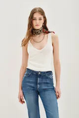 Musculosa de tejido de punto color blanco, con escote en V y breteles anchos. Presenta un diseño ajustado al cuerpo.