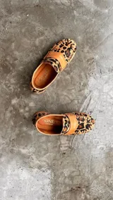 Mocasines de cuero en color dorado con detalles en marrón, con diseño bicolor y costuras artesanales expuestas en el empeine.