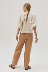 Blusa color crudo con bordado calado, cuello con volantes y lazos para ajustar. Mangas abullonadas con puños elásticos y lazos.