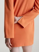 Vestido corto naranja de punto de algodón elástico con textura de canalé. Tiene cuello polo en V, mangas largas acampanadas e insignia con el monograma de Calvin Klein en el pecho.
