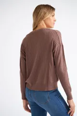 Cárdigan de tejido liviano con textura acanalada, cuello en V y cierre frontal con botones. Presenta mangas largas y un diseño clásico con detalle de grifa en cuero.