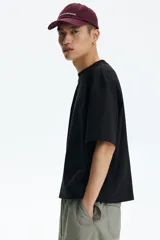 Remera negra de corte oversized y silueta holgada, confeccionada en punto liviano de algodón, con cuello redondo ribeteado y mangas cortas de hombros caídos.