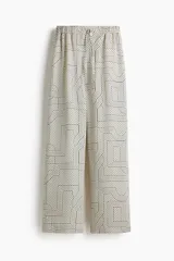 Pantalón de corte amplio y tiro alto, con cintura elástica y cordón de ajuste. Presenta un estampado geométrico en blanco y negro con líneas finas y formas entrelazadas.