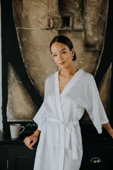 Bata tipo kimono de satén elastizado color blanco, con mangas al codo y largo por encima de la rodilla. Incluye un lazo de satén para ajustar en la cintura.