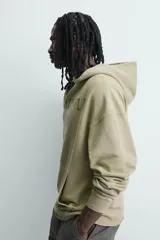 Sudadera de corte relajado color verde oliva con efecto lavado. Presenta capucha con abertura frontal, bolsillo tipo canguro, mangas largas con puños de rib y bajo con acabado irregular. Incluye estampado frontal con texto.