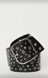 Cinto ancho de cuero sintético negro, con hebilla metálica plateada de forma cuadrada. La correa está decorada con múltiples tachas redondas y piramidales plateadas, además de ojales metálicos plateados a lo largo de toda su extensión.