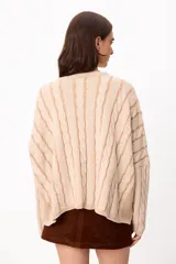 Sweater de punto con diseño de trenzas verticales, cuello redondo y corte crop. Presenta una combinación de colores crudo y camel, con mangas largas y ajuste holgado.
