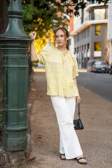 Blusa amarilla pastel de algodón con textura delicada, escote redondeado con lazo, mangas cortas abullonadas con volados y terminaciones sutiles.