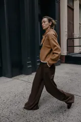 Jersey de punto color marrón, manga larga y corte holgado, con cuello tipo bandana anudado y terminaciones con puntilla blanca a contraste.