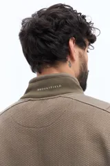 Campera de algodón con cierre frontal, cuello alto en color verde oliva y cuerpo texturado con patrón de espiga en tono marrón topo. Las mangas son lisas y del mismo tono que el cuerpo. Presenta un pequeño logo bordado en el pecho.