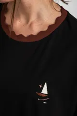 Vestido midi negro de algodón con mangas cortas, cuello redondo marrón con borde festoneado y pequeño bordado de velero en el pecho.
