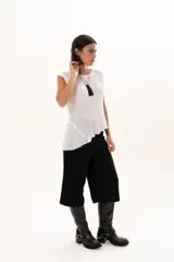 Blusa de textura rugosa en color blanco, sin mangas, con detalle de volados en los hombros y corte asimétrico en el ruedo.