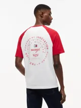 Remera de cuello redondo con diseño de mangas raglán en color rojo y cuerpo en color blanco. Presenta un estampado gráfico en el pecho con banderas de carreras y el logo de la colaboración Tommy Hilfiger x Cadillac Formula 1 Team.