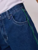 Bermuda de jean de mezclilla negra con efecto lavado, corte recto y costuras en contraste de hilo blanco. Presenta un parche bordado con el logo "Rusty" en color celeste en el bolsillo trasero derecho.