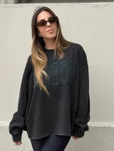 Buzo oversize de color negro con calce relajado y mangas amplias. Presenta letras en relieve con bordes desflecados en el frente y un ruedo inferior también desflecado.