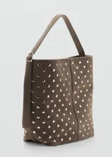 Bolso tipo hobo de gamuza marrón, adornado con tachas metálicas plateadas distribuidas por toda la superficie. Cuenta con una correa ajustable y cierre superior.
