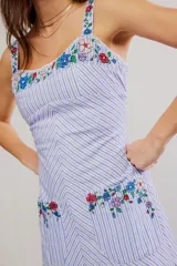 Vestido largo con diseño a rayas celestes y blancas, tirantes anchos, escote cuadrado y bolsillos frontales. Cuenta con delicados detalles de bordado floral multicolor en el pecho, tirantes y bolsillos.