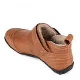 Botita baja Marcel confeccionada en cuero vacuno color marrón, con interior de corderito ultrasuave. Presenta costuras pespunteadas decorativas, tira lateral con hebilla metálica dorada y detalles de elástico negro. Suela plana de goma negra.