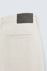 Bermuda color beige claro, de corte ancho y largo, confeccionada en algodón. Presenta cierre frontal con cremallera y botón, bolsillos laterales, bolsillo cerillero frontal y bolsillos traseros de vivo.