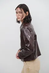 Chaqueta de efecto cuero brillante con acabado charol, cuello con solapas de piel sintética, cierre frontal con botones y bolsillos laterales.