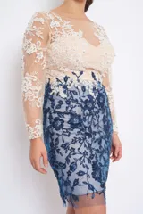 Vestido corto de fiesta con falda azul y parte superior color piel, ambos con bordado floral. El vestido tiene mangas largas transparentes con bordados y está confeccionado en tul con hilo y canutillos.