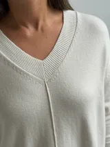 Sweater de punto color beige con escote en V, diseño holgado y costura central vertical. Presenta mangas largas con puños acanalados y ruedo con terminación acanalada.