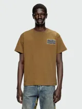 Remera de manga corta color marrón, con cuello redondo y un pequeño parche estampado con diseño abstracto en el pecho.