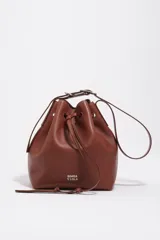 Bolso tipo saco de cuero marrón con cierre de cordón ajustable, asa larga regulable y logotipo de BIMBA Y LOLA impreso en el frente con letras blancas.