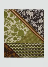 Pañuelo de tejido fluido de poliéster, con diseño estampado en bloques que combinan patrones florales, geométricos y franjas en tonos verde, marrón y negro, con terminaciones deshilachadas.
