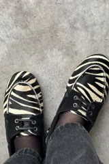 Mocasines tipo náuticos de cuero con estampado animal print de cebra y detalles en negro. Cuentan con cordones y ojales metálicos.
